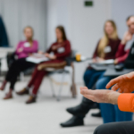 Menschen sitzen auf Stühlen in einem Halbkreis, Setting eines Seminars