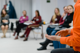 Menschen sitzen auf Stühlen in einem Halbkreis, Setting eines Seminars
