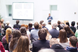 Vortragender mit Flipchart vor einer Masse sitzender Menschen